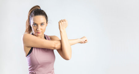 Determined young sporty woman stretching arm before workout on gray backgroundの写真素材