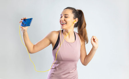 Sporty young woman in earphone holding smartphone and dancing over gray backgroundの写真素材