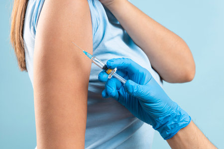 Young woman getting a vaccine on isolated blue background. Concept of vaccination in disease preventionの写真素材