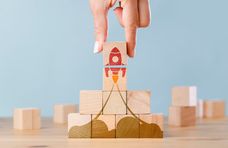 Hand arranging wooden cubes in a structure rocket shape. Conceptual of business startup and strategy.の写真素材
