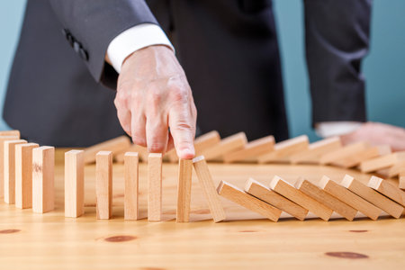 Businessman stopping wooden block from falling in the line of domino with risk concept