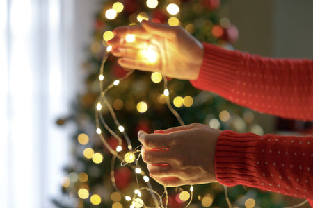 Woman's hands holding Christmas lights in front of sparkling Christmas treeの写真素材