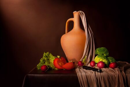 Flemish style lifestyle on brown background. Shot with studio lighting. Tomatoes, broccoli, ripe, knife and a jugの写真素材