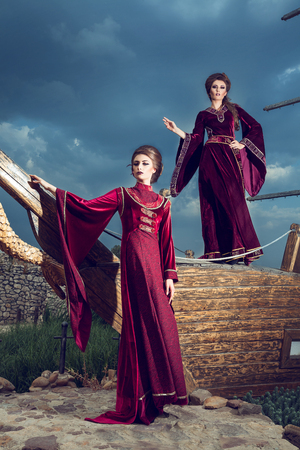 Two beautiful women dressed in vintage clothes in front of boat. Antique luxury. Retro clothes and vintage conceptの写真素材