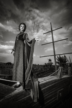 Woman in aristocratic clothes on boat in retro vintage concept. Elegancy and aristocracy. Rich woman from medieval period. Black and white imageの写真素材