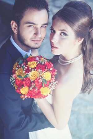 Happy married couple looking in camera. The bride has the bridal bouquet. Cold tonning. Artistic interpretationの写真素材