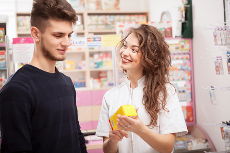 Pharmacist woman smiling and showing product to client inside pharmacy. Professional healthcare system. Healthcare businessの写真素材