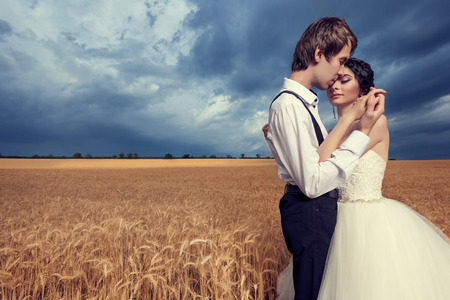 Loving bride and groom embracing each other in wheat field with dramatic blue sky and yellow wheat. Love and happines. Married couple. Wedding dayの写真素材