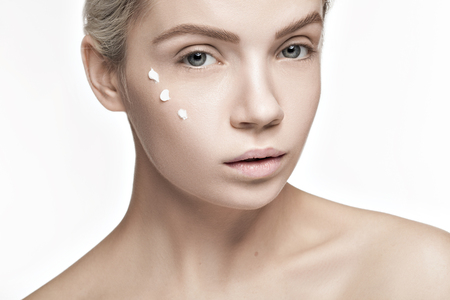 Cream and beauty. Woman with drops of cream on face looking at cameraの写真素材