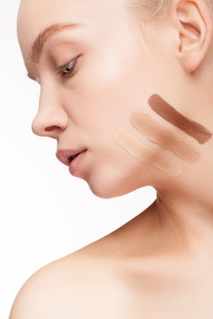 Testing cosmetic products. Young woman testing cosmetic products on her skin on white background in studioの写真素材