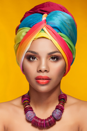 Young woman with afro american turban on yellow background in studio photo. Beauty and make up. Traditions and cultureの写真素材