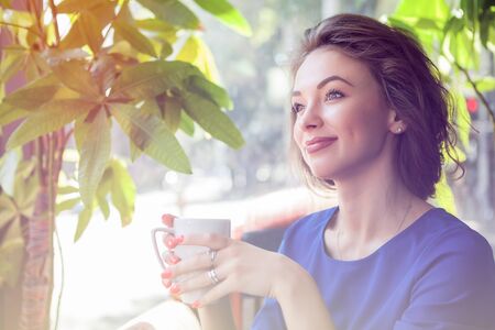 Woman in interior holfing a cup of coffe in hands and looking away from the cameraの写真素材