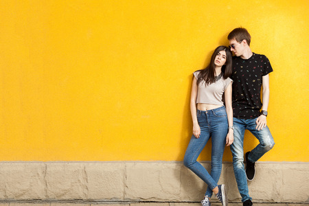 Younf woman and men posing in fashion jeans style outside on yellow wallの写真素材
