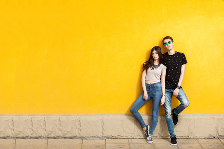 Couple posing in fashion jeans style to the camera on yellow wallの写真素材