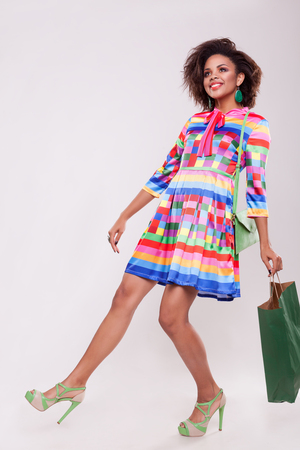Cute afro american young woman with a shooping bag in hand on grey background in studio photoの写真素材