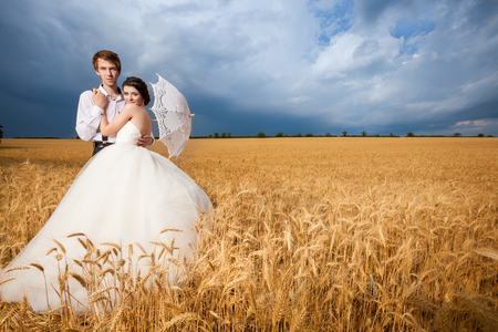 Young bride and groom in fantastic wheat field and dramatic sky. Perfect wedding. Wedding photography. Happy just maried coupleの写真素材