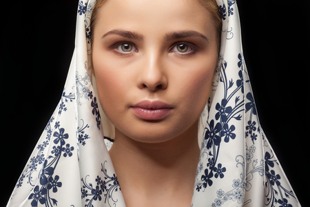 Beautiful woman with headscarf on her head on black background in studio photoの写真素材