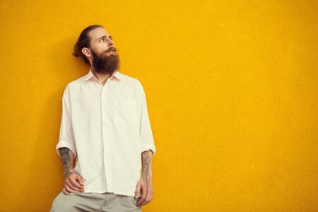 Bearded and tattooed man posing on yellow wall outside. Fashion and styleの写真素材