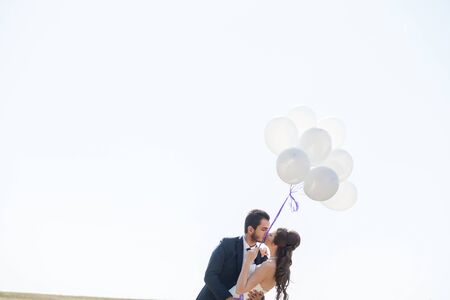 Happy just married couple with balloons in hand on white skyの写真素材