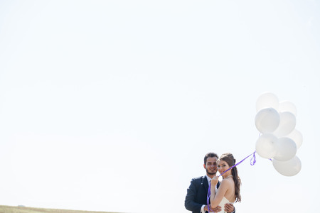 Happy just married couple with balloons in hand on white skyの写真素材