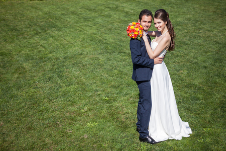 Embracing wife and groom on grass field in sunny summer day. Just married couple. Wedding photographyの写真素材
