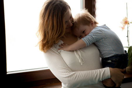 Mother and her sleepy baby boy with a window in backgound. Happy childhood and parentingの写真素材