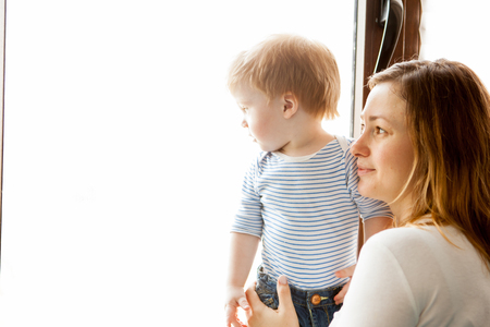 Mother with her beautiful baby boy looking at the window. Happy childhood and parentingの写真素材