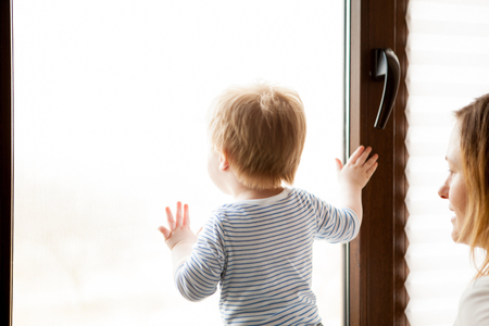 Mother with her beautiful baby boy looking at the window. Happy childhood and parentingの写真素材
