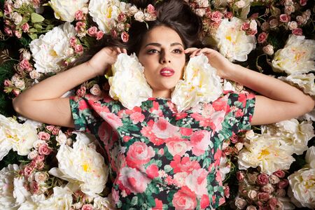 Portrait of beautiful sensual woman lying down on flowers in studio photo. Beauty concept. Floral decorationの写真素材