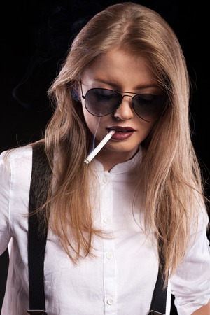 Blonde woman smoking on black background in studio photoの写真素材