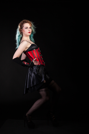 Sensual woman in fetish red leather corset on black background in studio photo. BDSM and dominatrixの写真素材