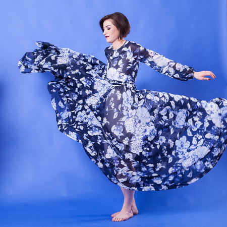 Model with long flying dress on blue background in studio photo. Elegance and beautyの写真素材
