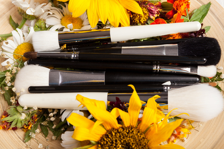 Make up brushes on plate next to wild flowers on wooden backgroundの写真素材