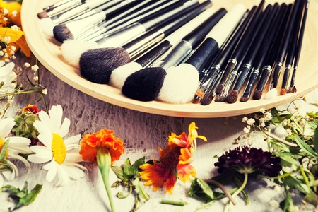 Professional Make up brushes on plate next to wild flowers on wooden backgroundの写真素材