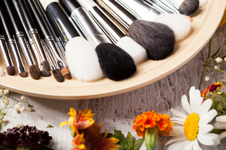 Professional Make up brushes on plate next to wild flowers on wooden backgroundの写真素材