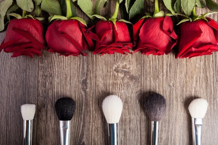 Conceptual image of make-up brushes next to roses on wooden backgroundの写真素材