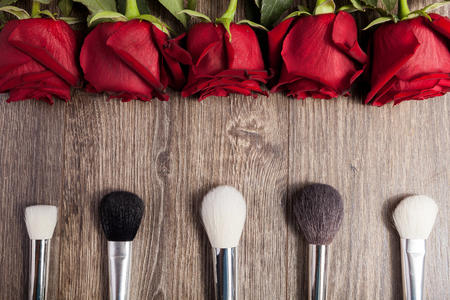 Conceptual image of make-up brushes next to roses on wooden backgroundの写真素材