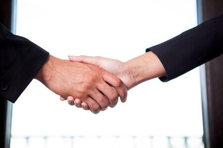 Businesswoman and businessman shaking hands on window backgroundの写真素材