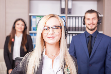 Portrait of beautiful blonde from customer support line next to two colleaguesの写真素材