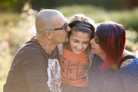 Father and mother kissing their daughter in the parkの写真素材