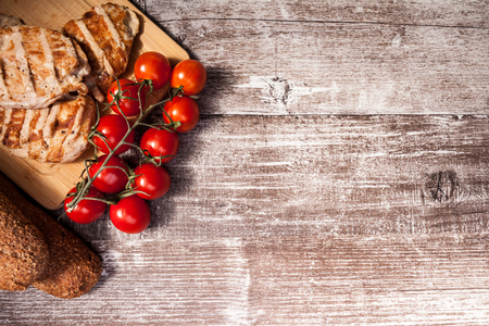 Delicious grilled chicken on wooden board next to healthy bread, tomatoes and salad. Healthy lifestyle and eatingの写真素材