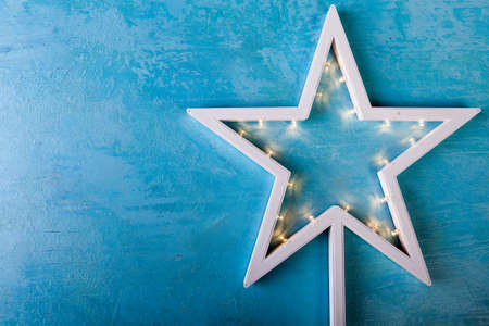 White Christmas star with yellow lights on blue wooden background in studio photoの写真素材