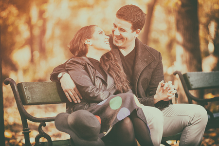 Happy couple sitting on a bench in autumn parkの写真素材