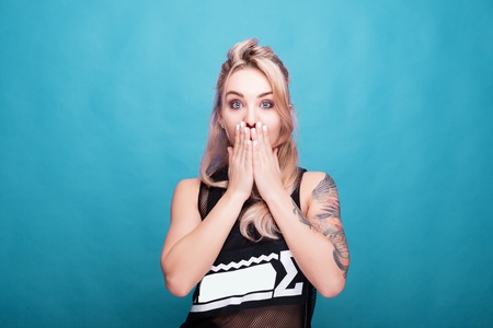 Surprised woman with her hands covering the face looking straight to the camera. Studio photo on...