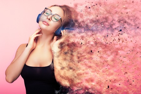 Conceptual image of woman listening to music while she is being dispersed in small particles from...