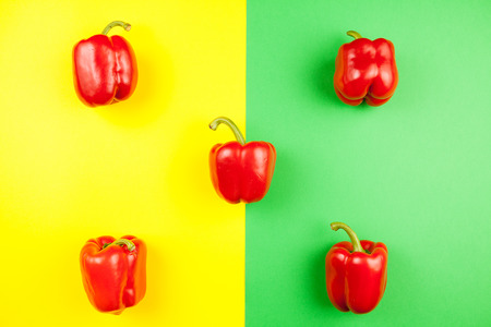 Top view on five fresh sweet red peppers on two colored background in yellow and greenの写真素材
