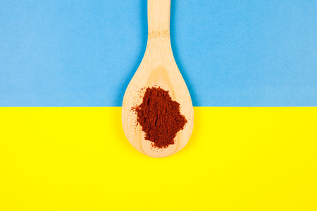 Top view on wooden spoon with powder chili over two colored background in yellow and blueの写真素材