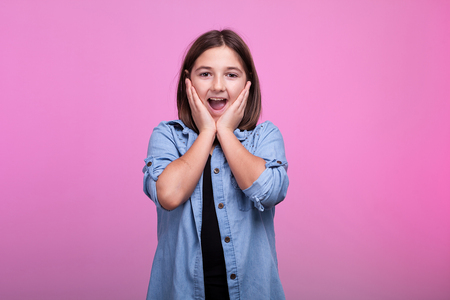 Suprised girl holding her hands on the face on pink background in studioの写真素材