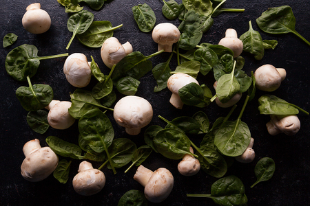 Top view on mushrooms and baby spinach on dark wooden tableの写真素材