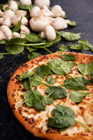 Pizza covered with spinach leaves next to mushrooms on dark wooden backgroundの写真素材